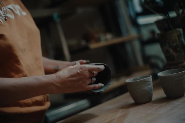 A persons hand shaping a cup out of gray clay
