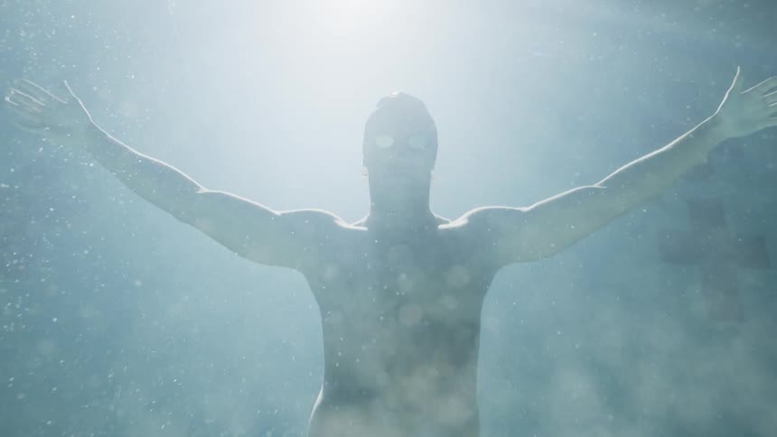 Submerged man with hands up returning to the surface of the pool