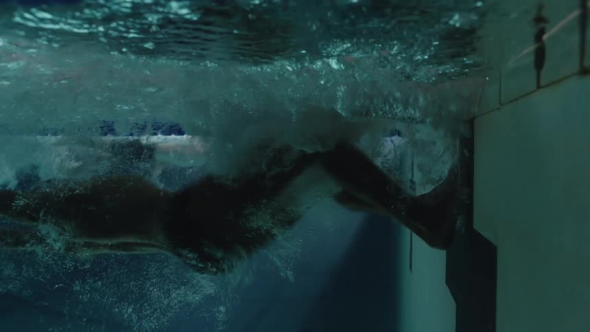 Underwater view of a pool with two swimmers kicking their legs on the corner of the wall and performing the maneuver and continuing to swim