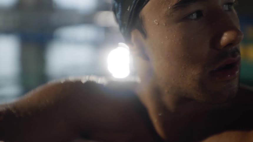 Man with swimming cap and goggles at the edge of the pool taking a deep breath