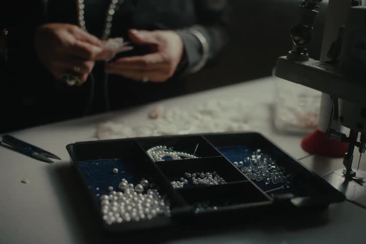 A person is making a necklace using some pearls that are in a little black box