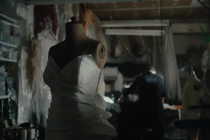Mannequin wearing a white dress in a sewing studio with a man working in the background