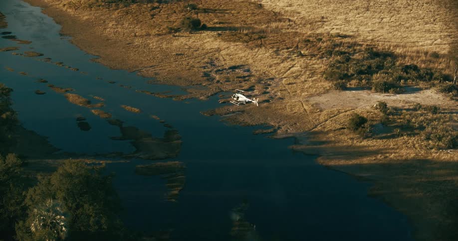A helicopter flies over a river next to a grassland