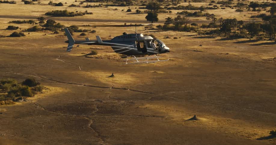 A helicopter flies over a vast savanna dotted with trees