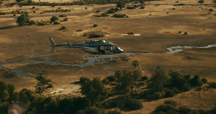 Helicopter flying over a vast open field with sparse trees and winding rivers