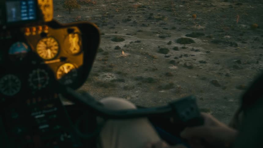 Persons hand controlling a helicopter moving close to the ground of a savanna
