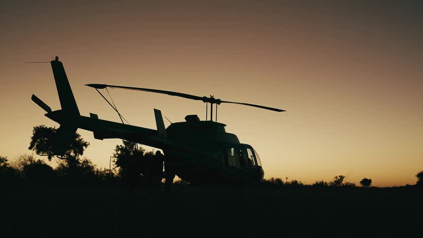 Person silhouetted against a red sky moves around a helicopter likewise silhouetted