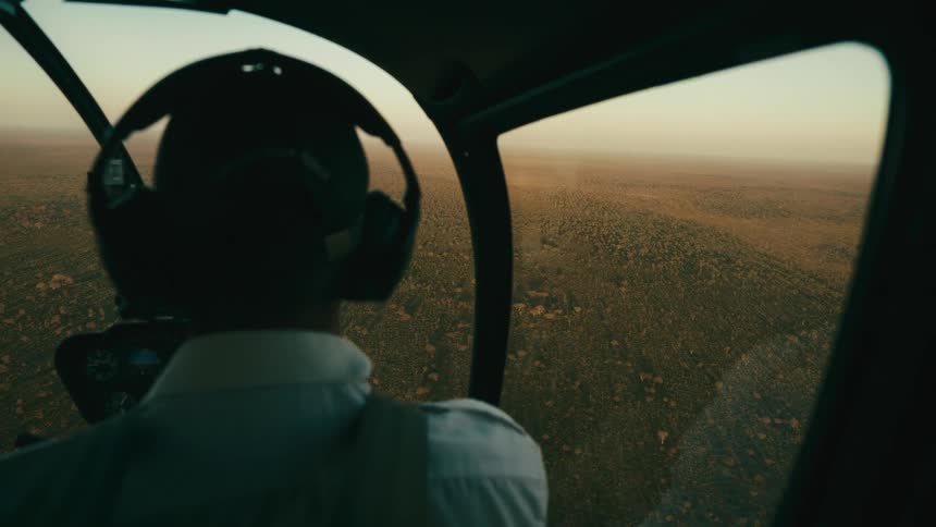 Inside view of a helicopter cockpit with a pilot flying above a jungle