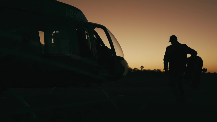 Man silhouetted against the afterglow after dusk carries a door to the side of a parked helicopter
