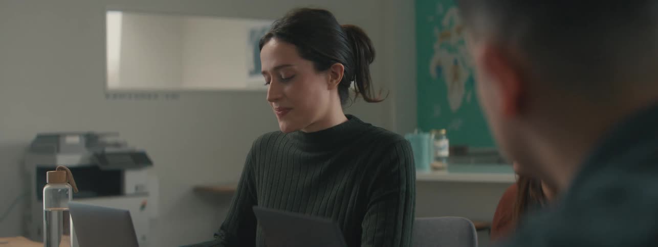 Three colleagues sitting at a table talking and using a laptop