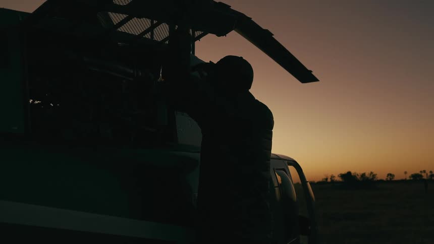 A silhouette of a person using a flashlight to see part of a helicopter that is resting on the ground in a dark morning environment