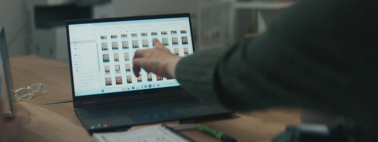 Two women sitting at a wooden work table with one of them turning her laptop towards the other to show her a series of images