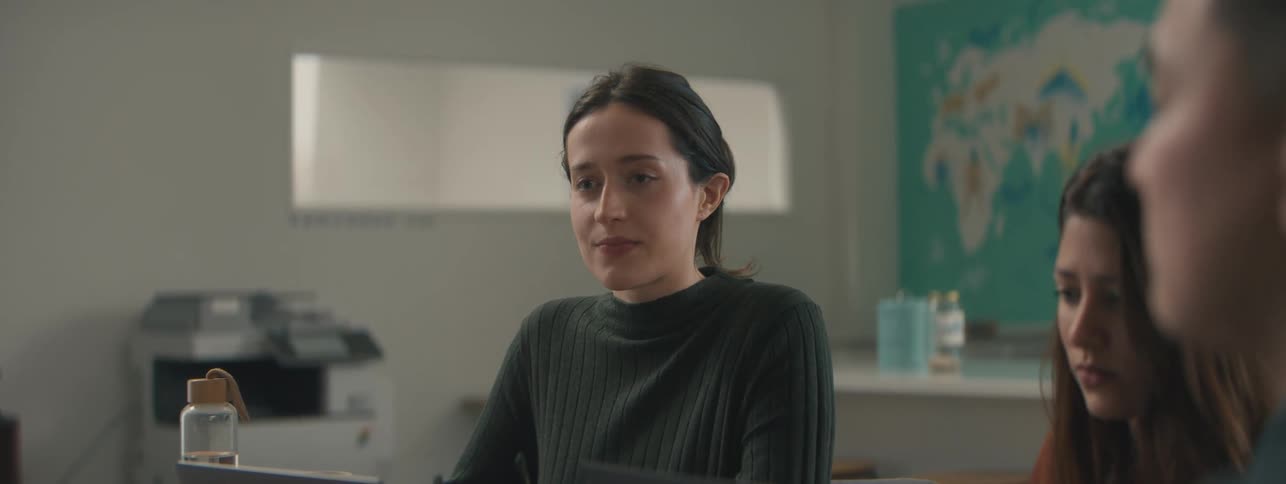 A woman is using her laptop because she is at a table and there are two people next to her and then she takes off her reading glasses and becomes thoughtful
