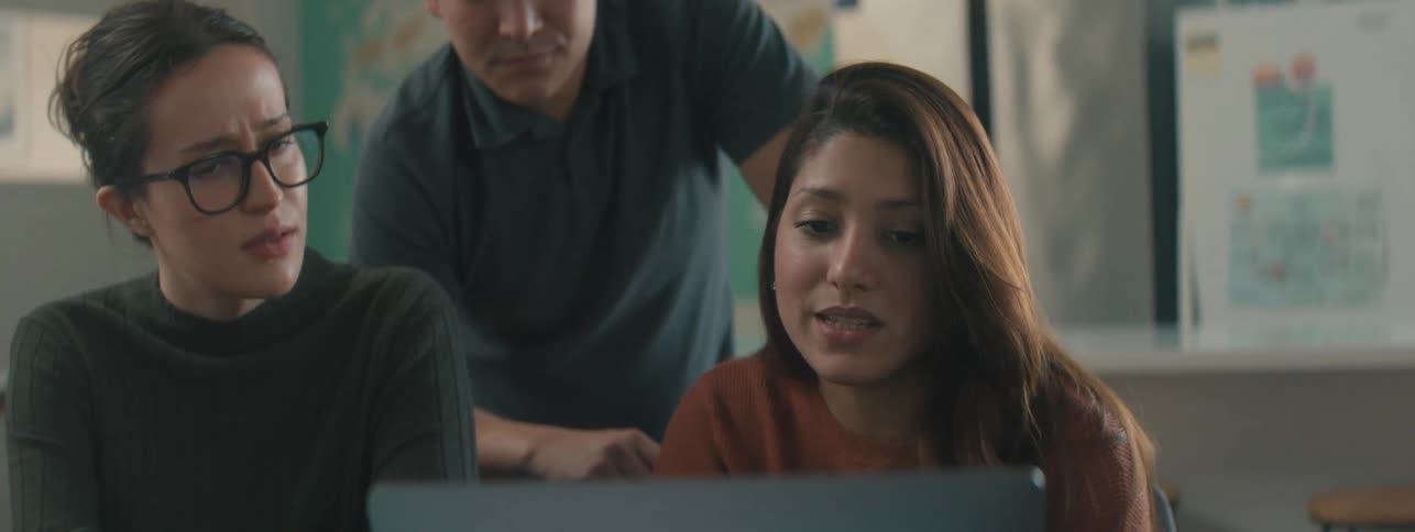Three students have a discussion while looking at a laptop screen