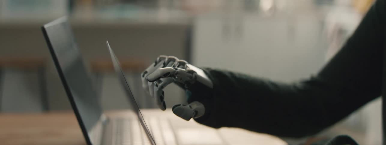 Two office coworkers one of them with a prosthetic hand collaborate while using their laptops