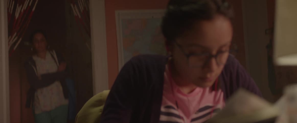 Woman sits at a desk writing and another woman walks in to look