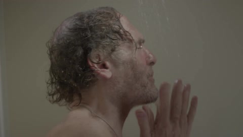 A man in the shower cleaning his face