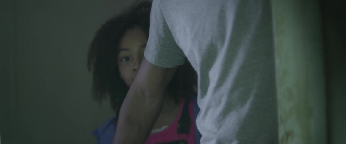 A young girl peaks around a corner as a teenage boy blocks her with his arm