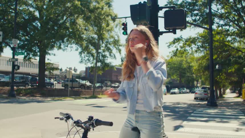 A teenage girl puts a ear bud in and rides off down a sidewalk on a bike