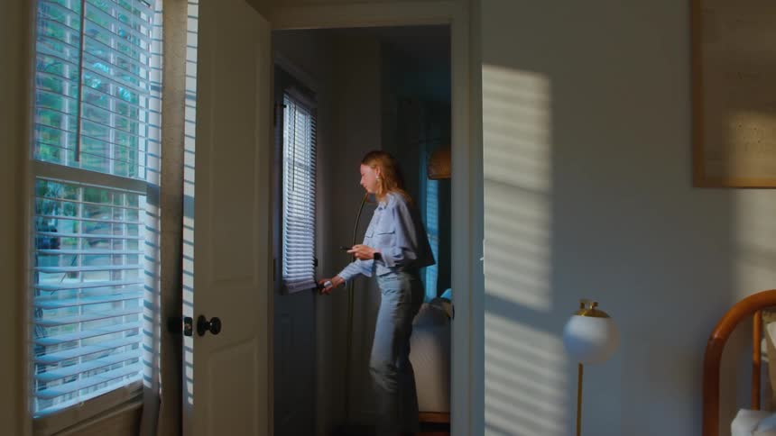 A teenage girl walks through a house and exits through a door