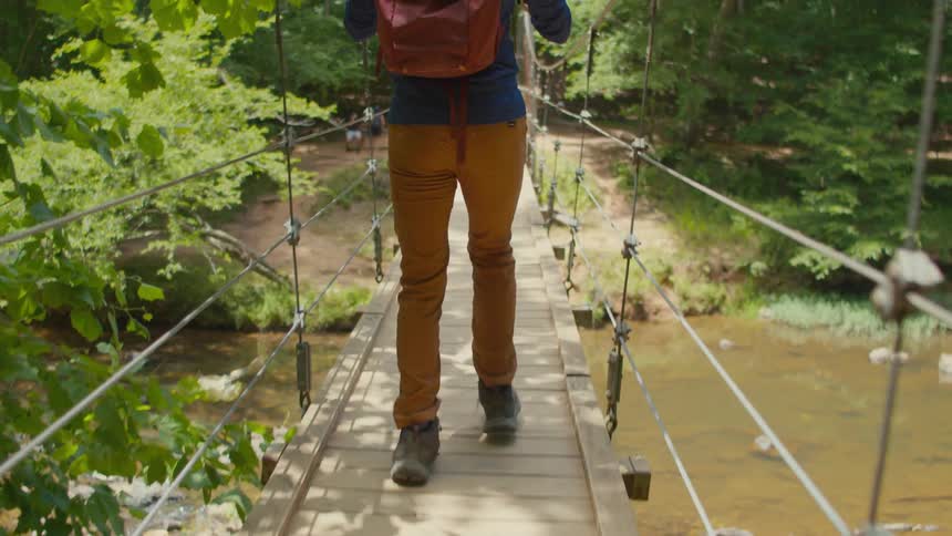 A man hikes over the small wood bridge