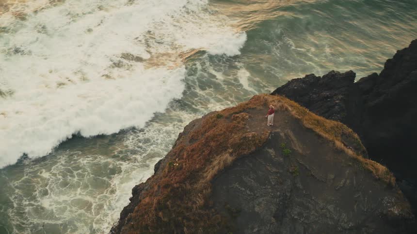 A solitary figure stands on a rocky promontory overlooking a vast ocean