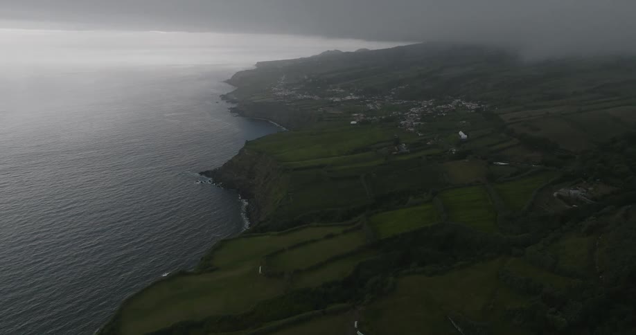 Aerial view of a coastline stretching into the distance with lush green fields at sunset under low clouds