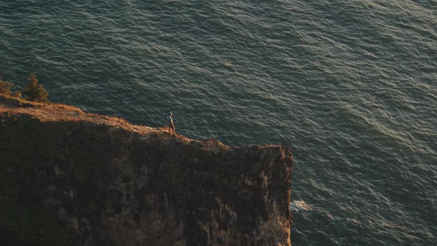 A man stands on a coastal peak and looks out over the ocean