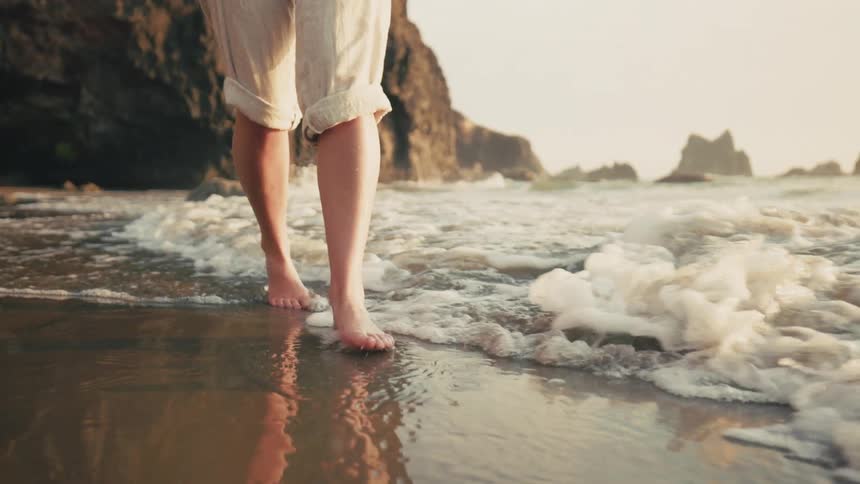 Legs of a barefoot woman walking on the sand and water of the beach
