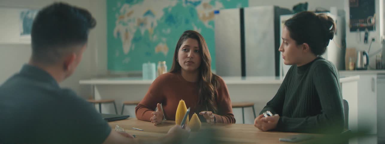 Two women and a man talking at a table with abstract yellow objects