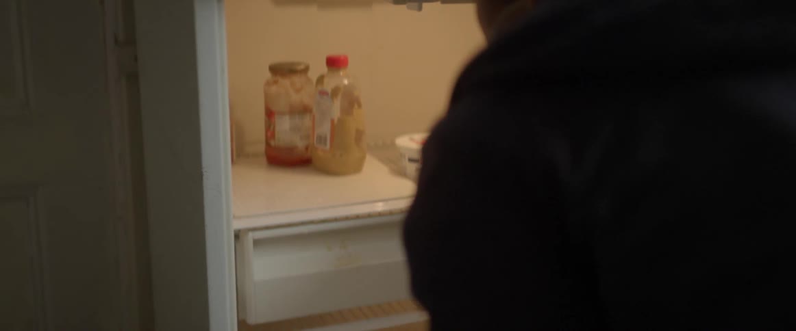 A woman looking in a empty refrigerator and getting something out