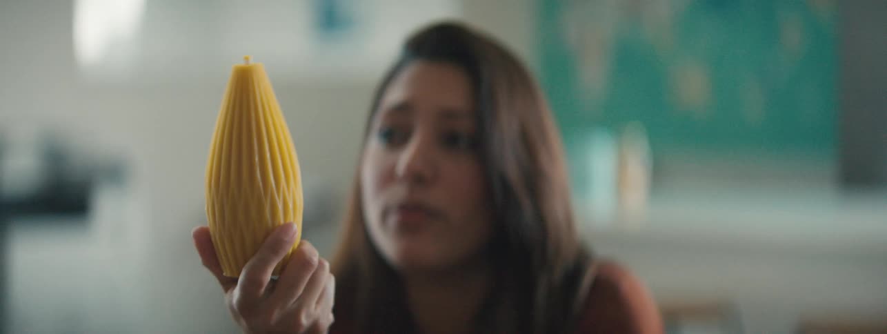 A woman holding a yellow oval 3d printed shape and inspecting it
