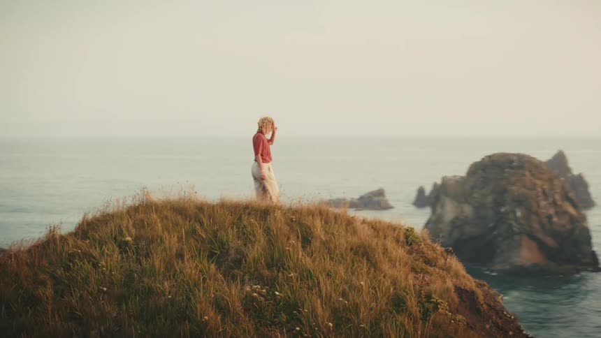 Blonde woman walking on the peak of a seaside hill