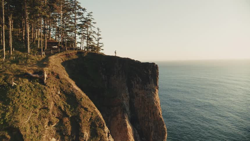A man walks out on a trail on top of a mountain coast line