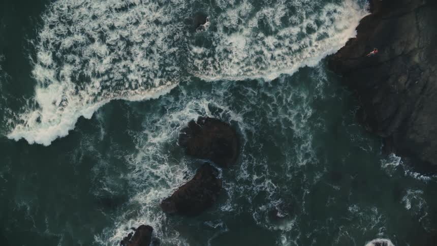 Person sits on promontory as waves crash against its base