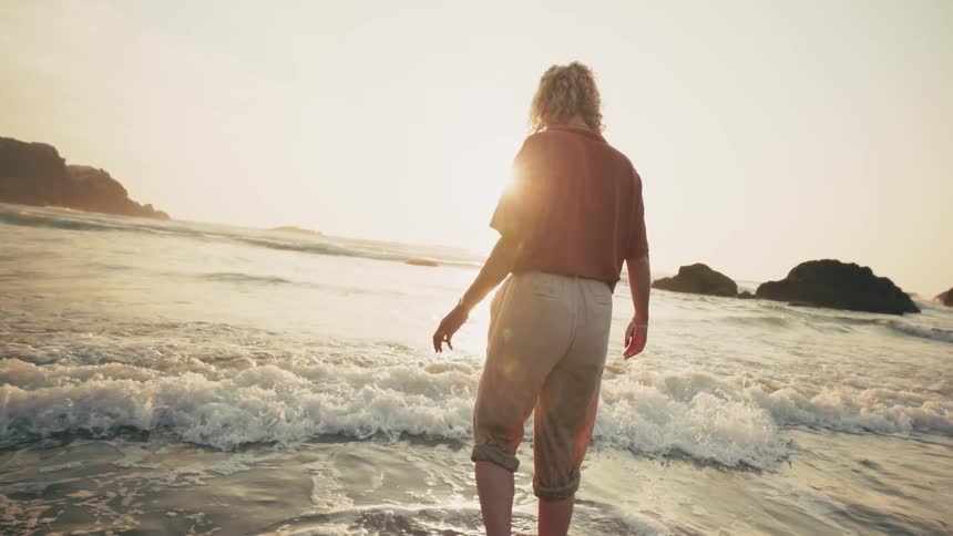 Someone on a beach with their feet in the water while fully dressed and walking further into the sea