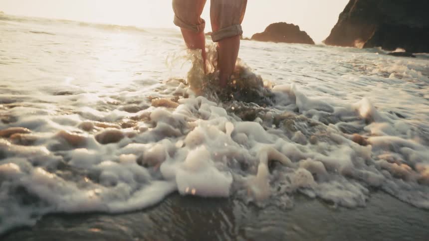 Person with their pants rolled up wades in the surf