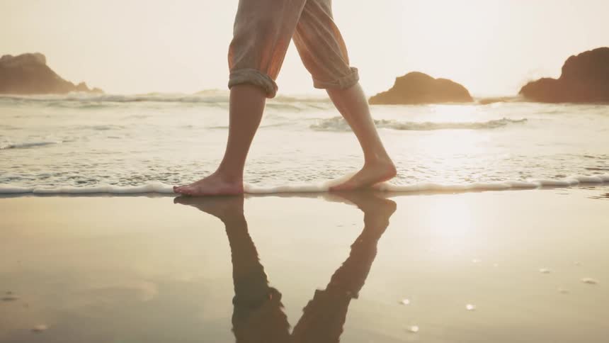 A person walks barefoot on the beach at sunrise