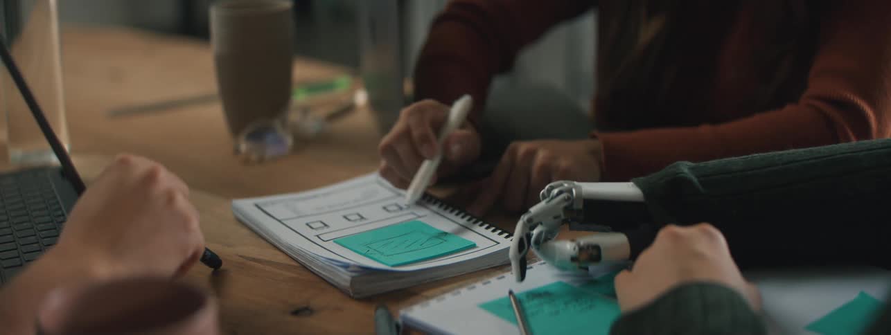 People sitting at a table with one of them pointing to a document and writing