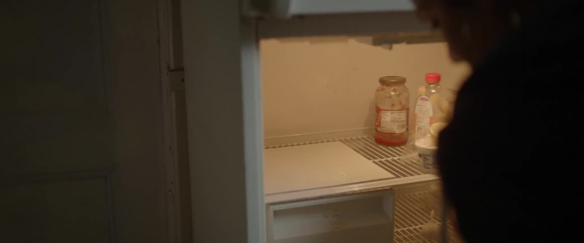 A woman pulls a small tin foil package out of an empty refrigerator