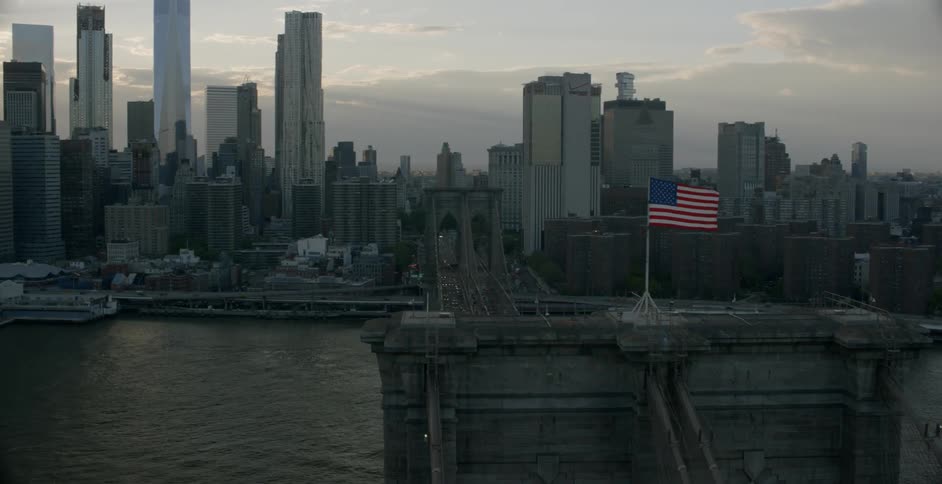 The american flag flies on top of a bridge in the city at dawn