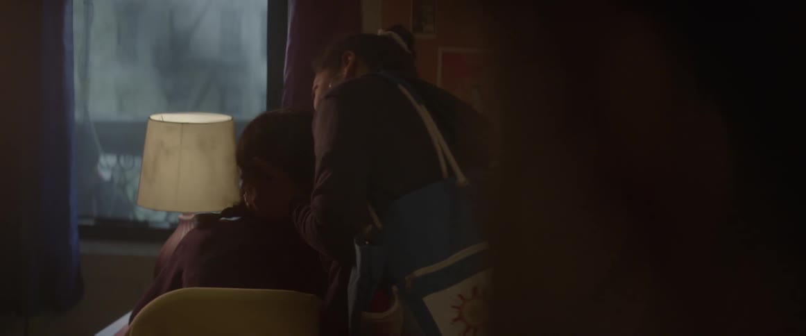 A woman rubs a person's shoulder and kisses their head