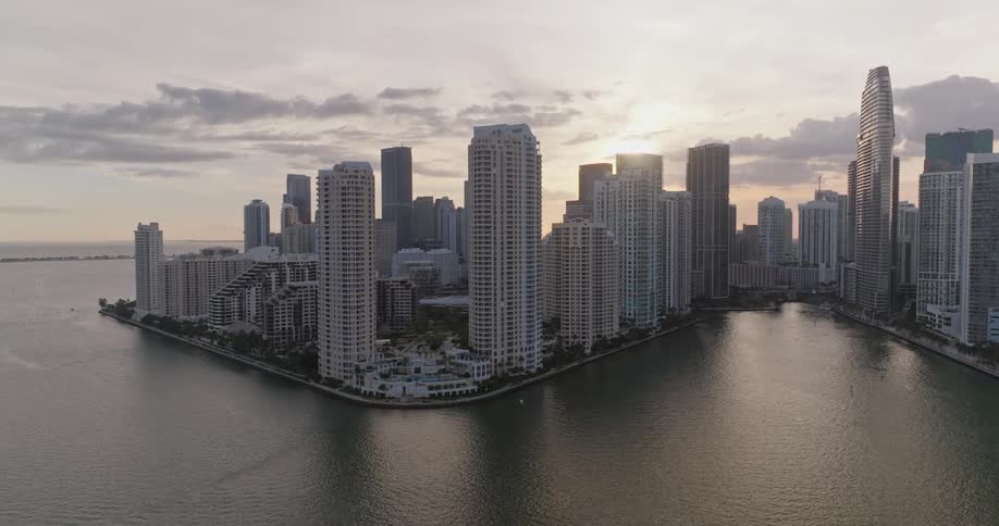 Aerial view of a metropolis with skyscrapers on the seafront and the sun on the horizon
