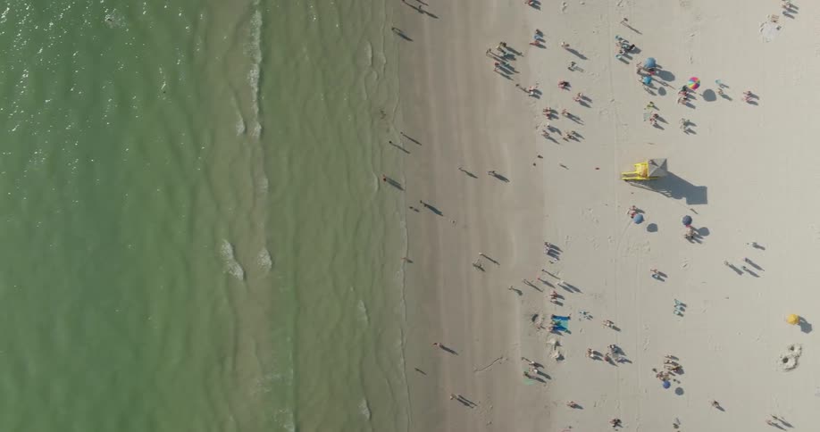 Aerial view of a beach with greenish water and white sand full of people