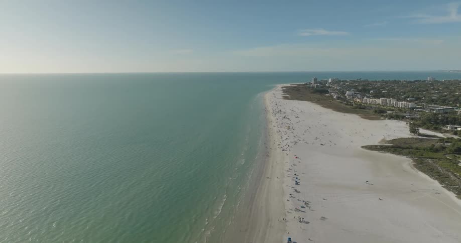 An aerial view of a beach with many people on the sand on the shore and an immensity of the sea to the horizon
