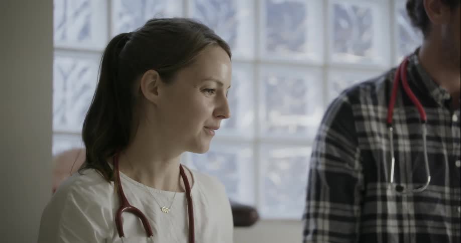 A man and woman with stethoscopes are being talked to in a lobby