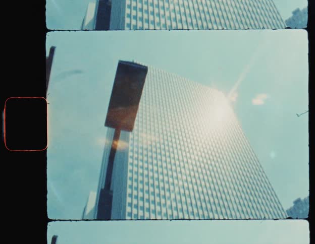 A low angle view of a tall modern skyscraper against a bright sun drenched sky