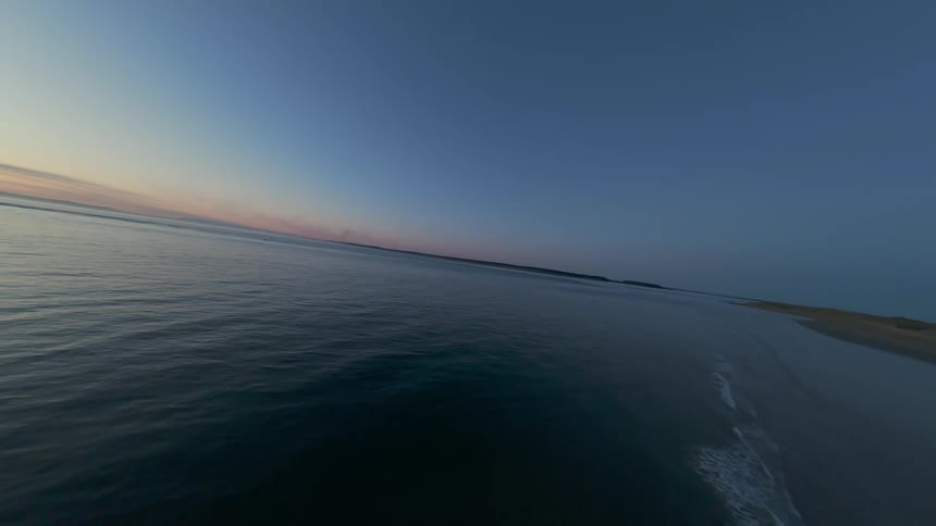 Aerial FPV drone view of a beach on a dark dawn with moody light and calm waves