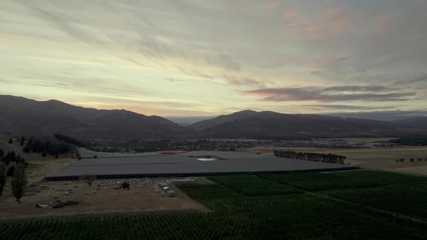Aerial shot of a flat area in a rural countryside with the silhouette of mountains and a city in the background