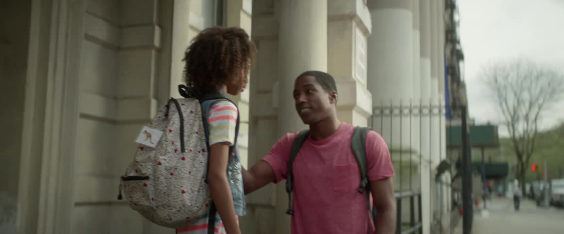 A teenage boy talks to his little sister outside a building during the day